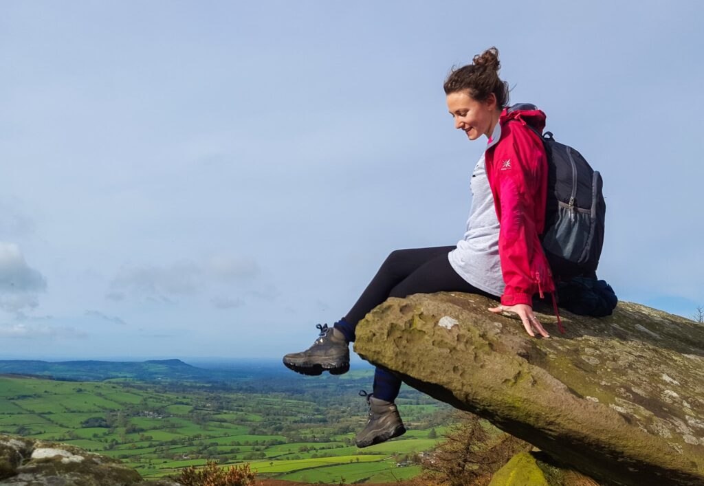 A girl in a pink rain coat sat on a precarious ledge in the Roaches, Derbyshire