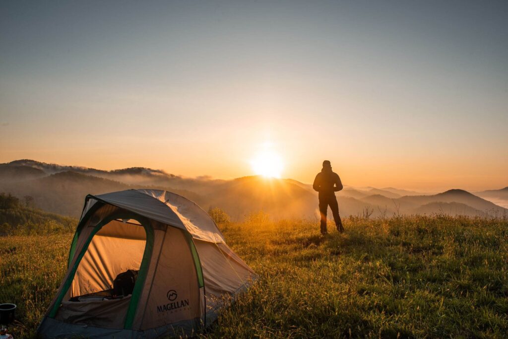 A man watching the sunset with a tent pitched on a hill