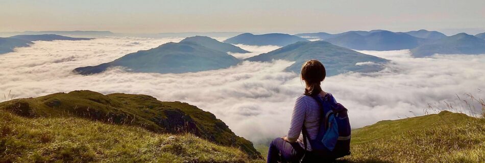 a woman on the top of a munro looking at mountain tops in cloud