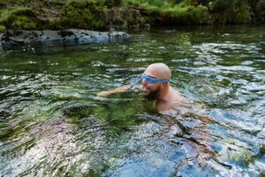 A bald man with goggles on swimming in an outdoor plunge pool