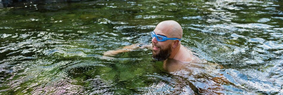 A bald man with goggles on swimming in an outdoor plunge pool